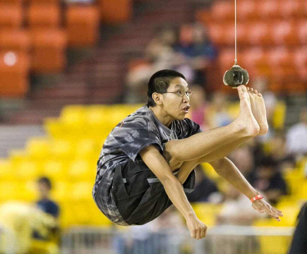 A young man has both feet high in the air and aiming toward a suspended ball.
