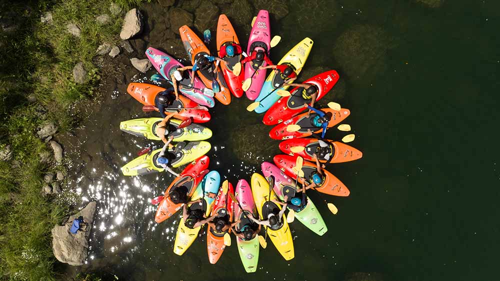 Several kayaks of various colors are arranged in a circle on the river.
