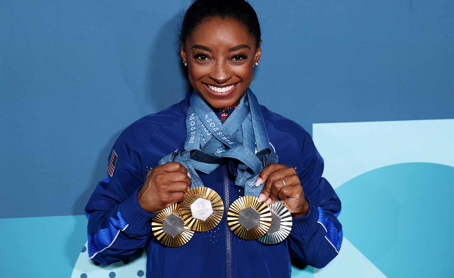 Simone Biles smiles while wearing four Olympic medals around her neck.