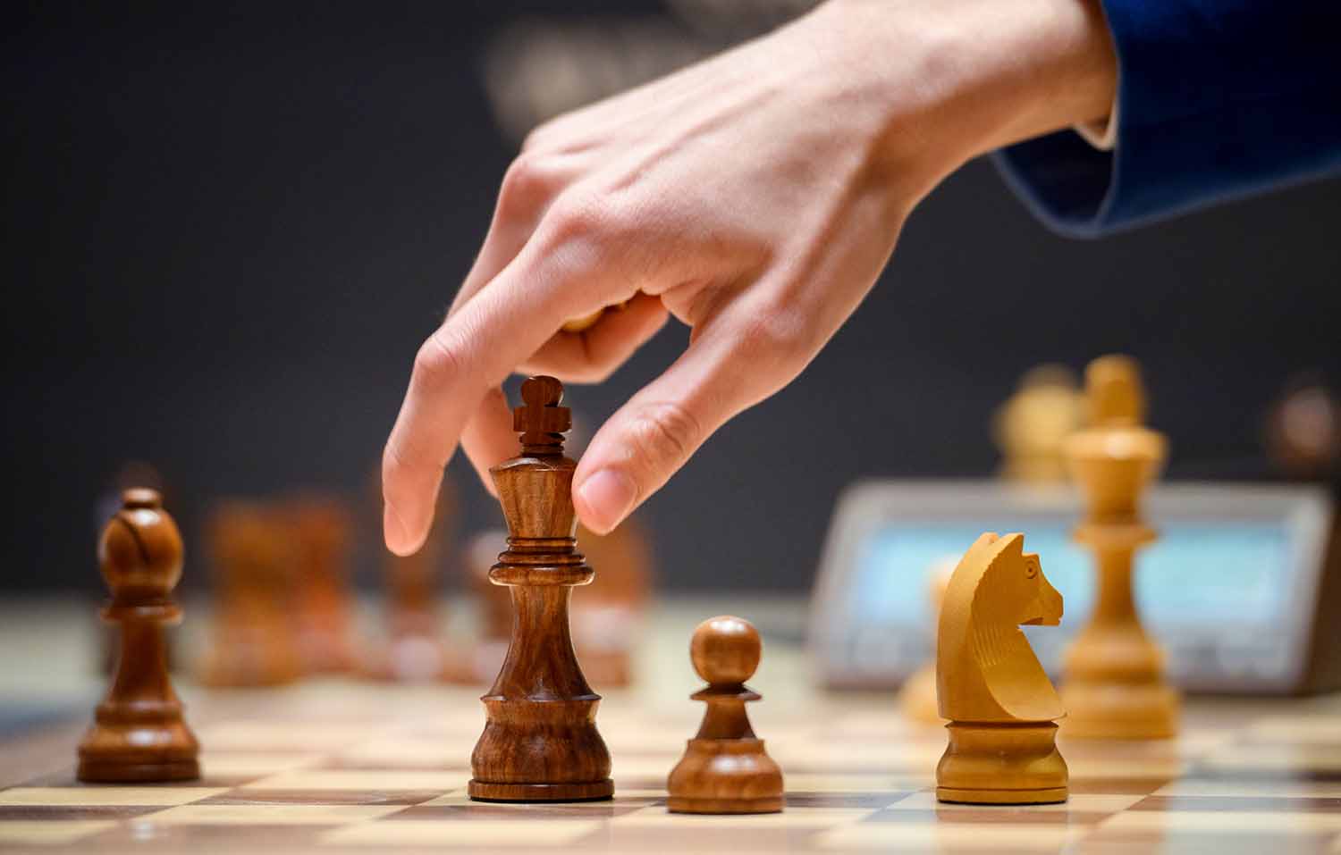 A hand hovers over a chess piece on a chessboard in the middle of a game.