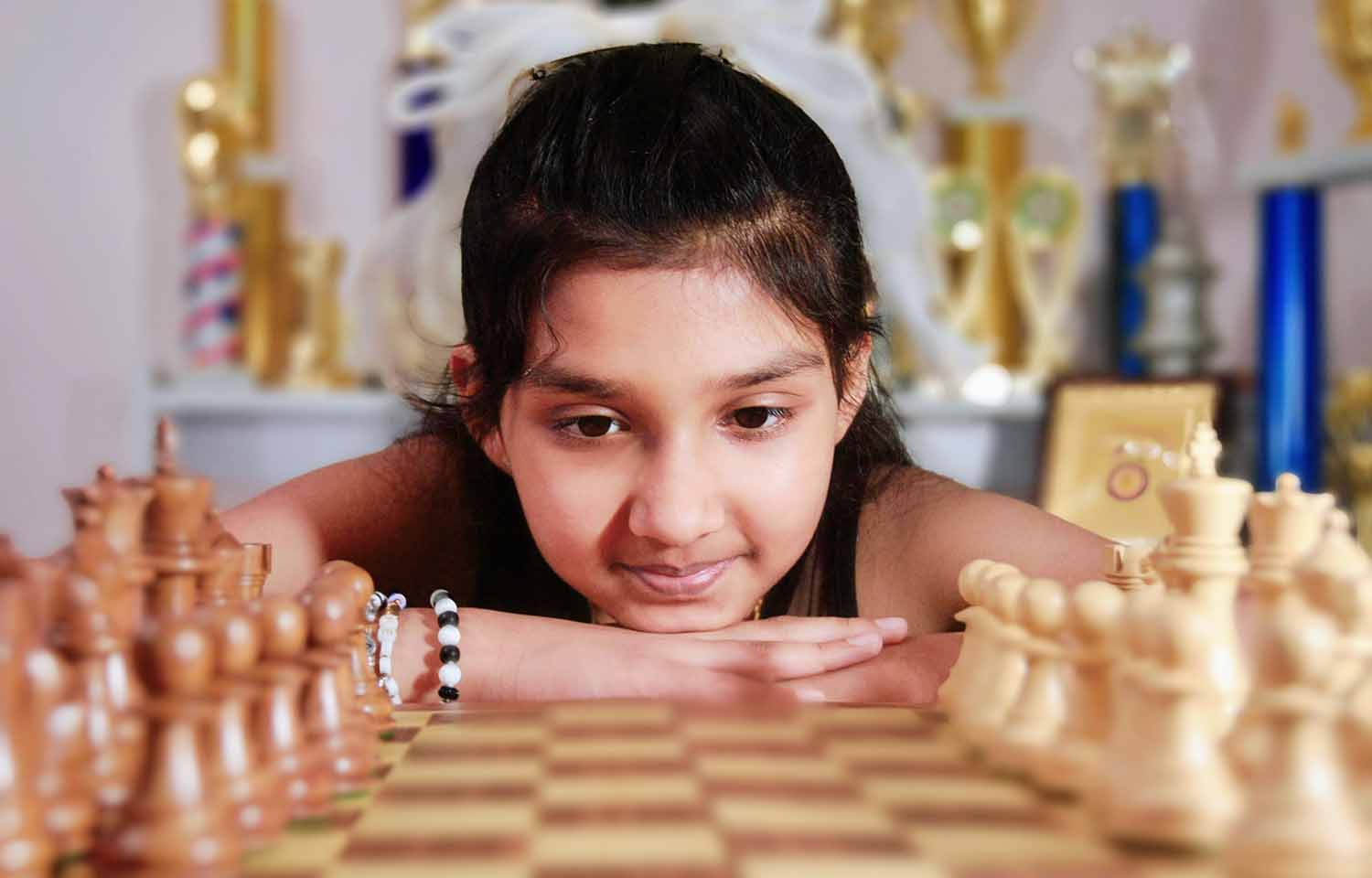 Keya Jha poses with her head at the level of a chessboard that has been set up for a game.
