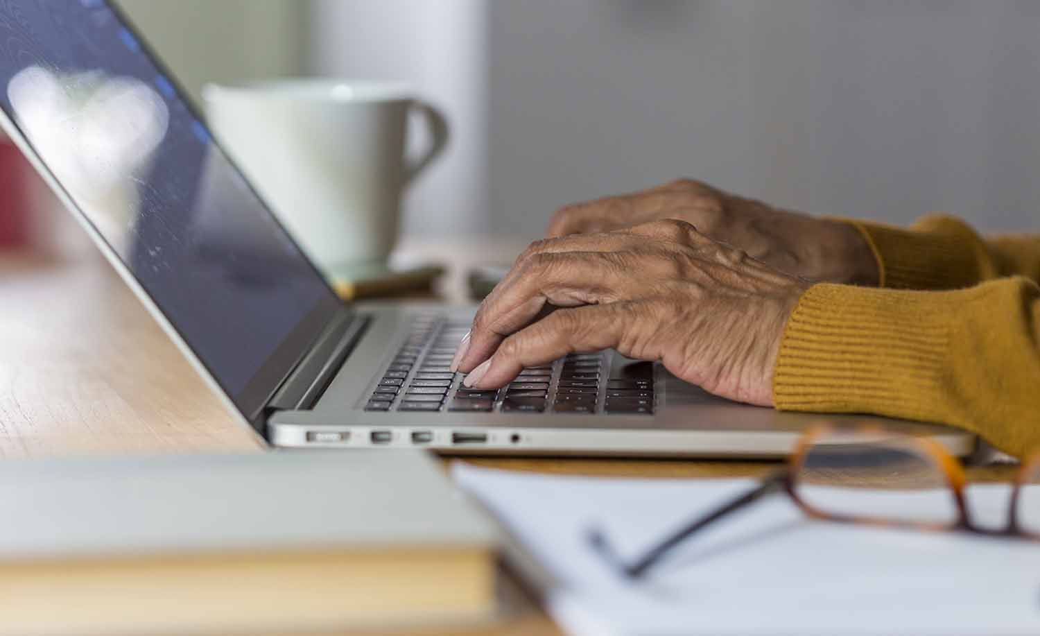 The hands of an older person are shown using a computer keyboard.
