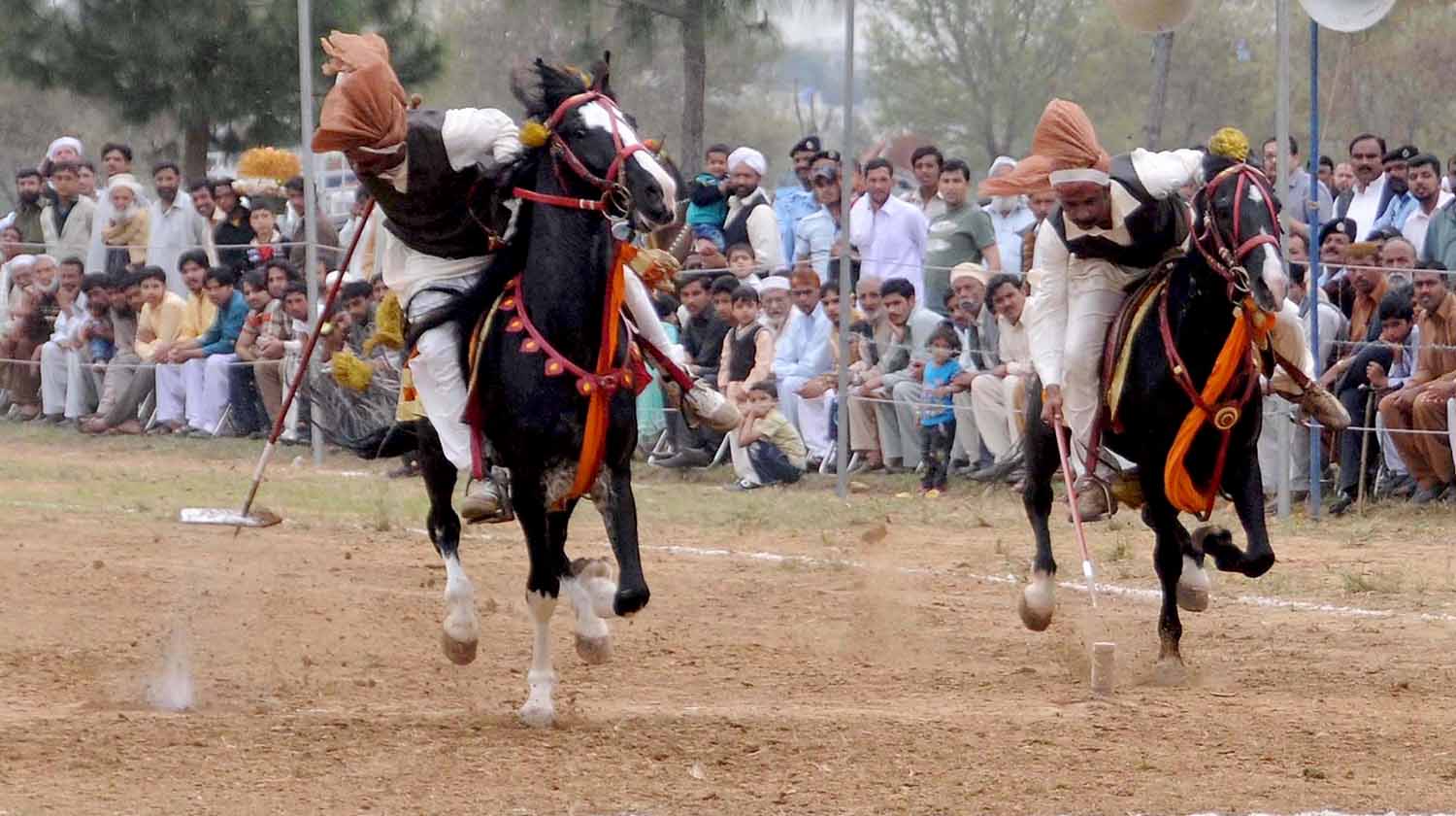 Two men riding decorated horses attempt to stab ground targets with spears.