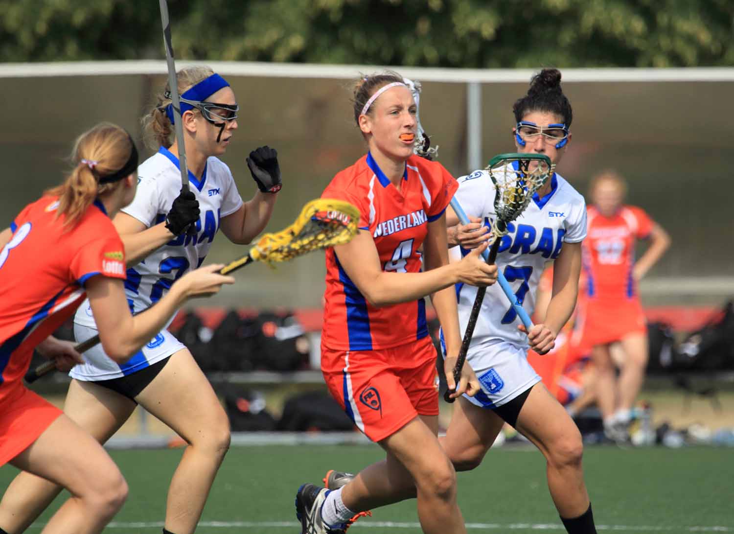 Players from two teams carry their lacrosse sticks as they run across the field during a game.