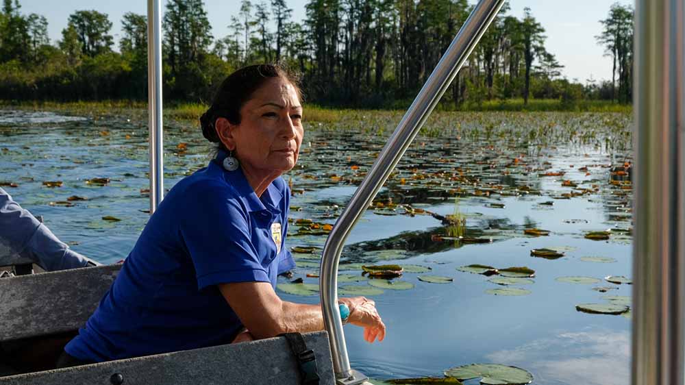 Former Secretary of State Deb Haaland leans out of a boat on a body of water.