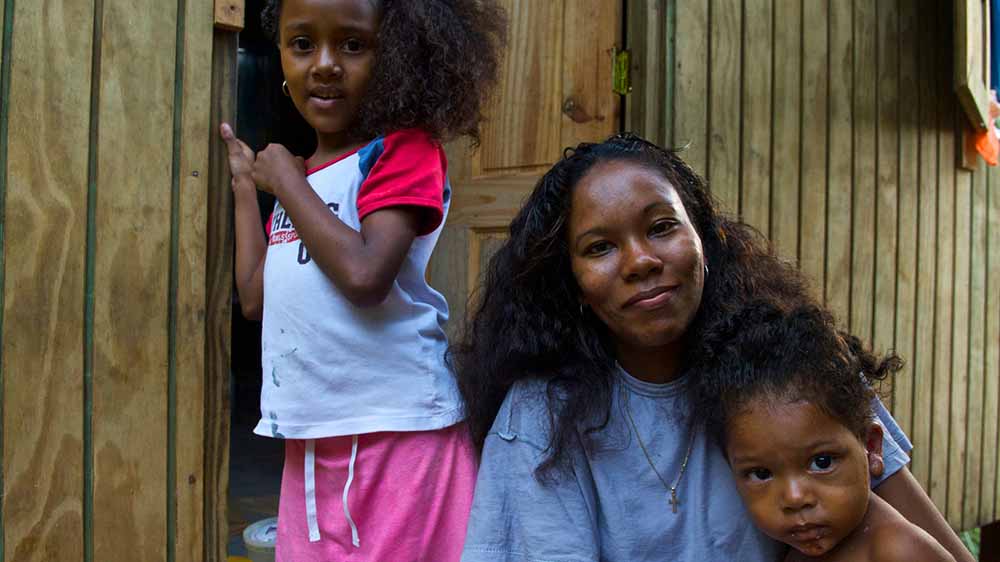 A woman poses with two children in front of a door to a structure.