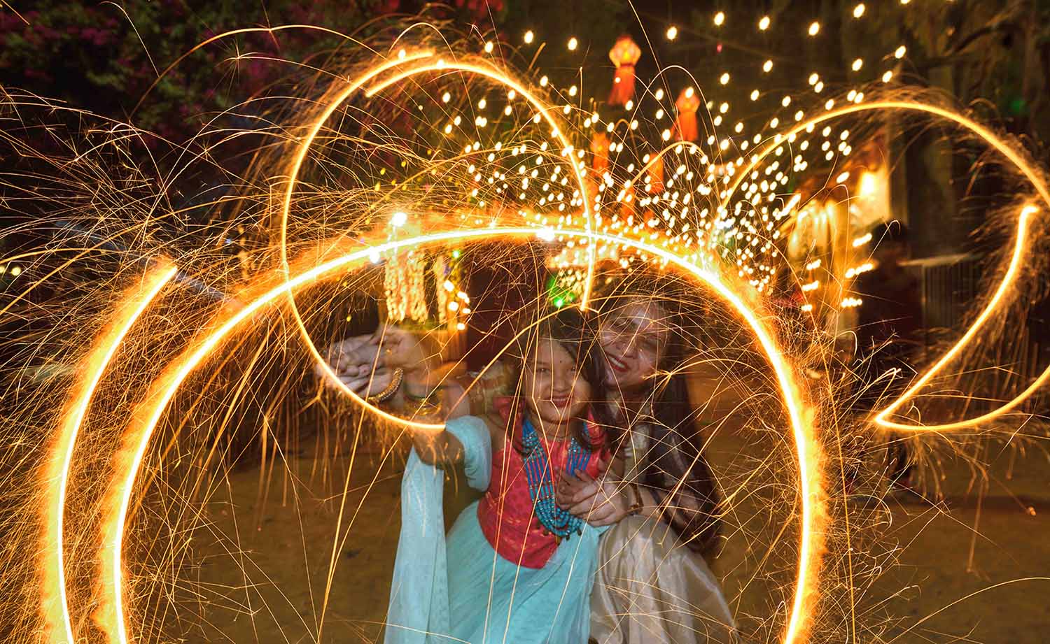 A woman and a young girl smile at the camera while surrounded by fireworks outdoors at night.