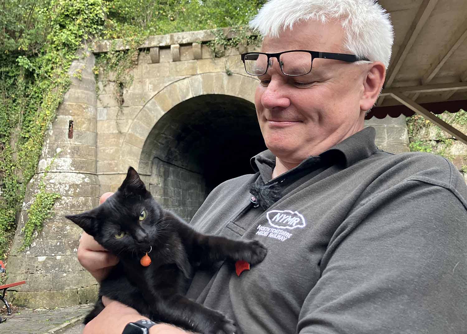 Simon Wall holds a black kitten while wearing a North Yorkshire Moors Railway jacket.