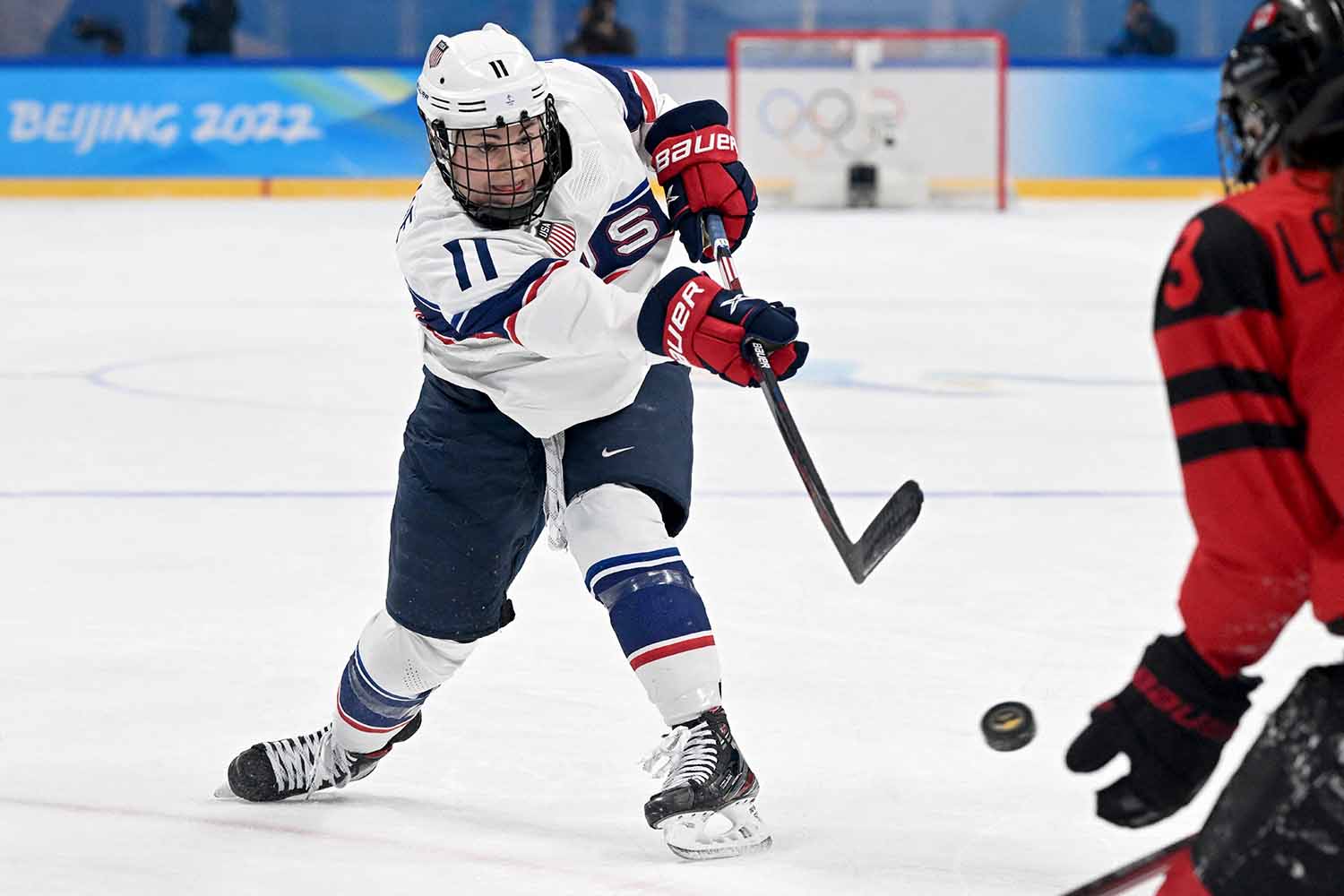 Abby Roque shoots a puck during a hockey game as an opposing player watches the puck.