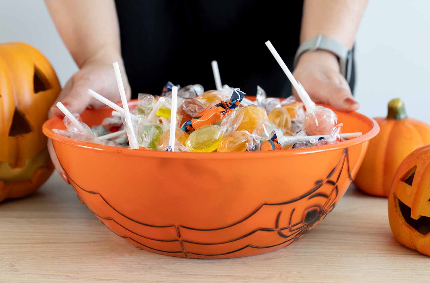 A candy-filled orange bowl with a spider web design is held by two hands.