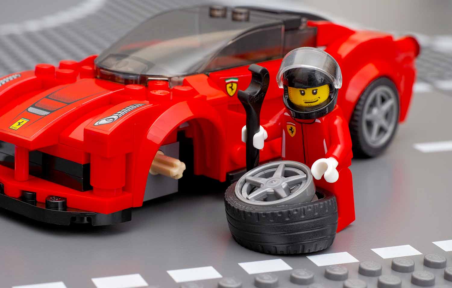 A LEGO mechanic figure is posed in front of a LEGO car holding a wrench as if it is about to put a tire onto the car.