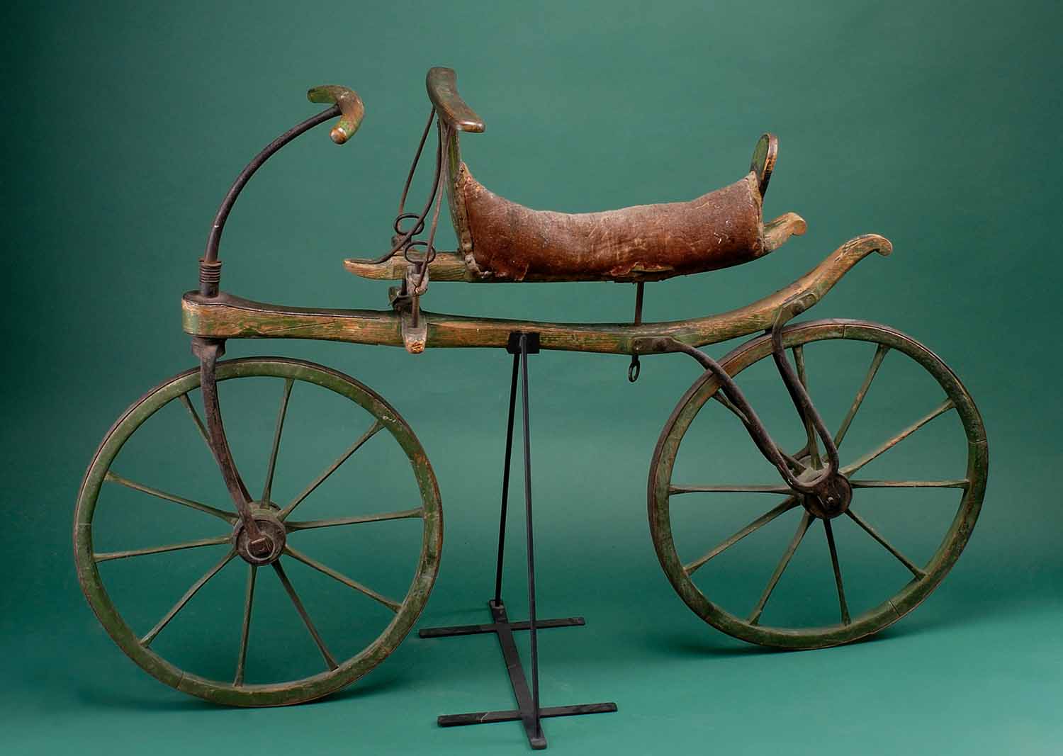 A Laufmaschine, a bike with a wooden frame and no pedals, is propped on a metal stand.
