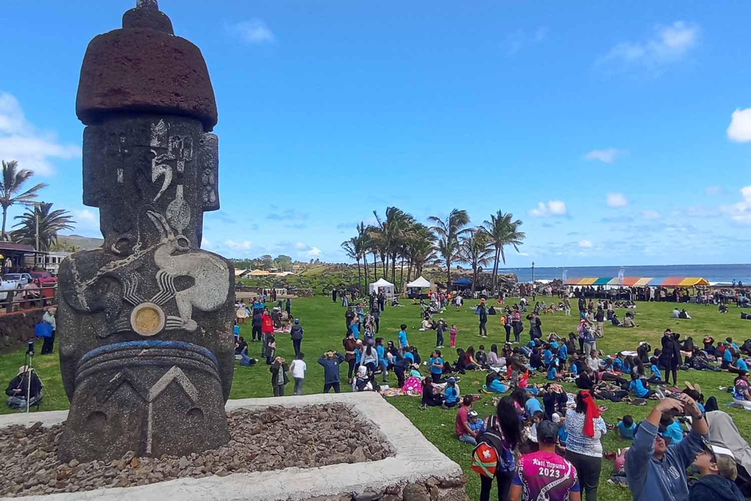 A giant statue is perched over an open space where a crowd of people are using eclipse glasses to look at the sky.