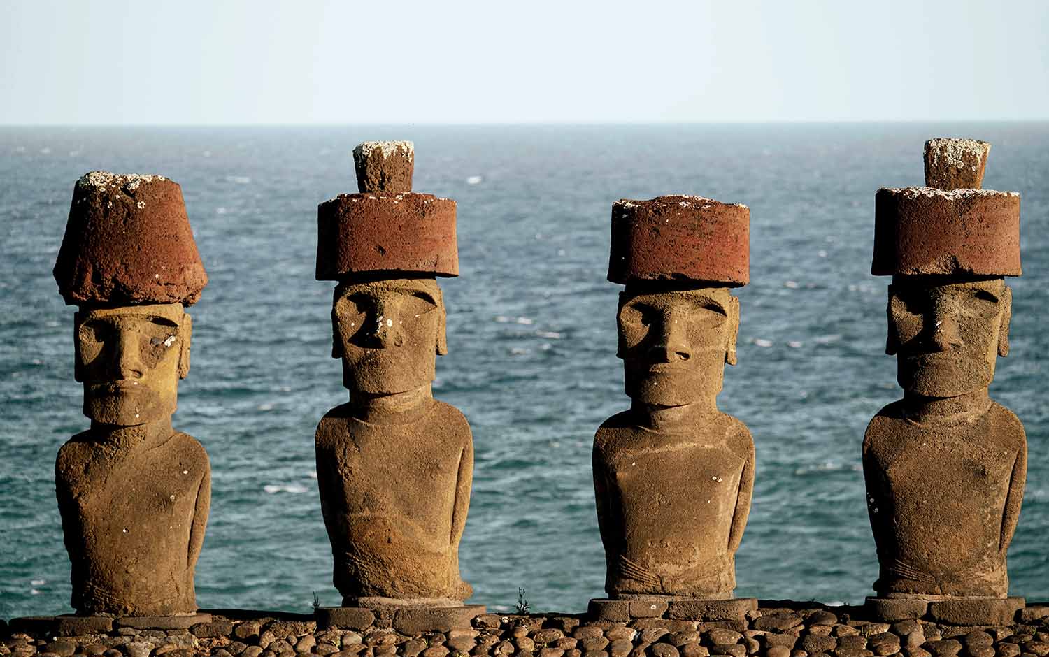 Four moai statues stand in a row and are visible from the waist up with the sea in the background.