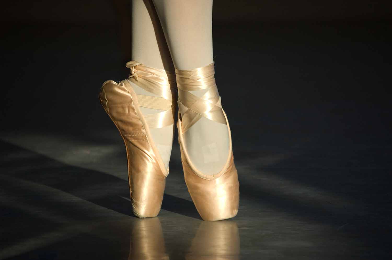 A closeup shows feet dancing in pointe shoes.