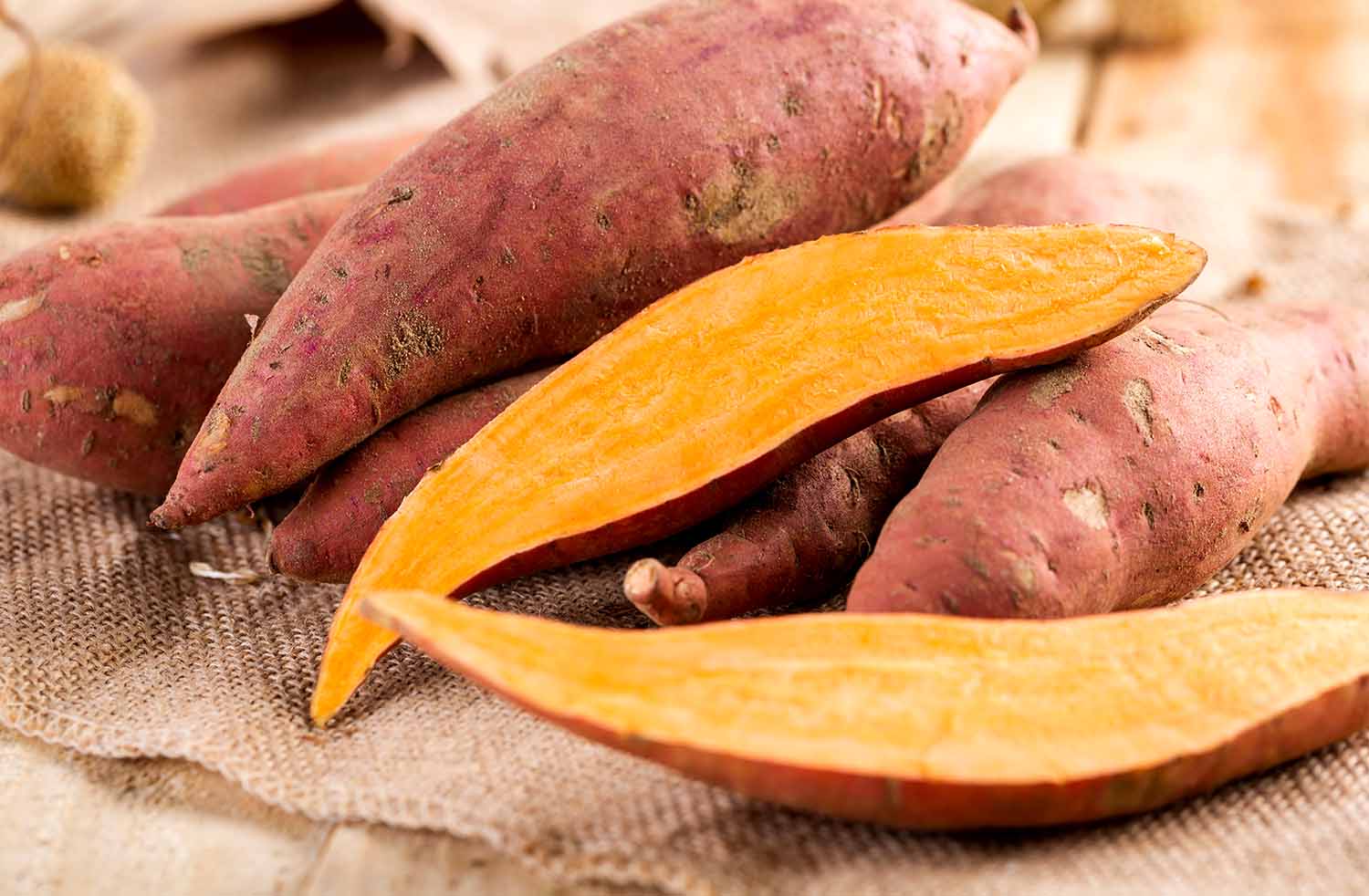 Whole and cut up sweet potatoes rest on a cloth.