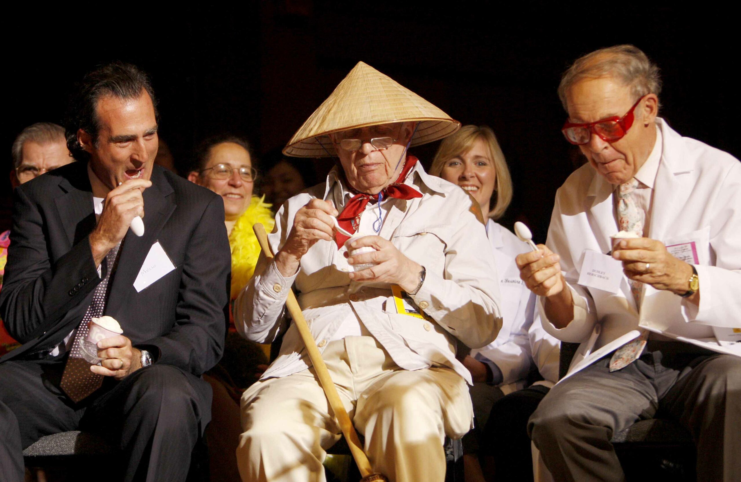 Three men sit in an audience and eat ice cream.