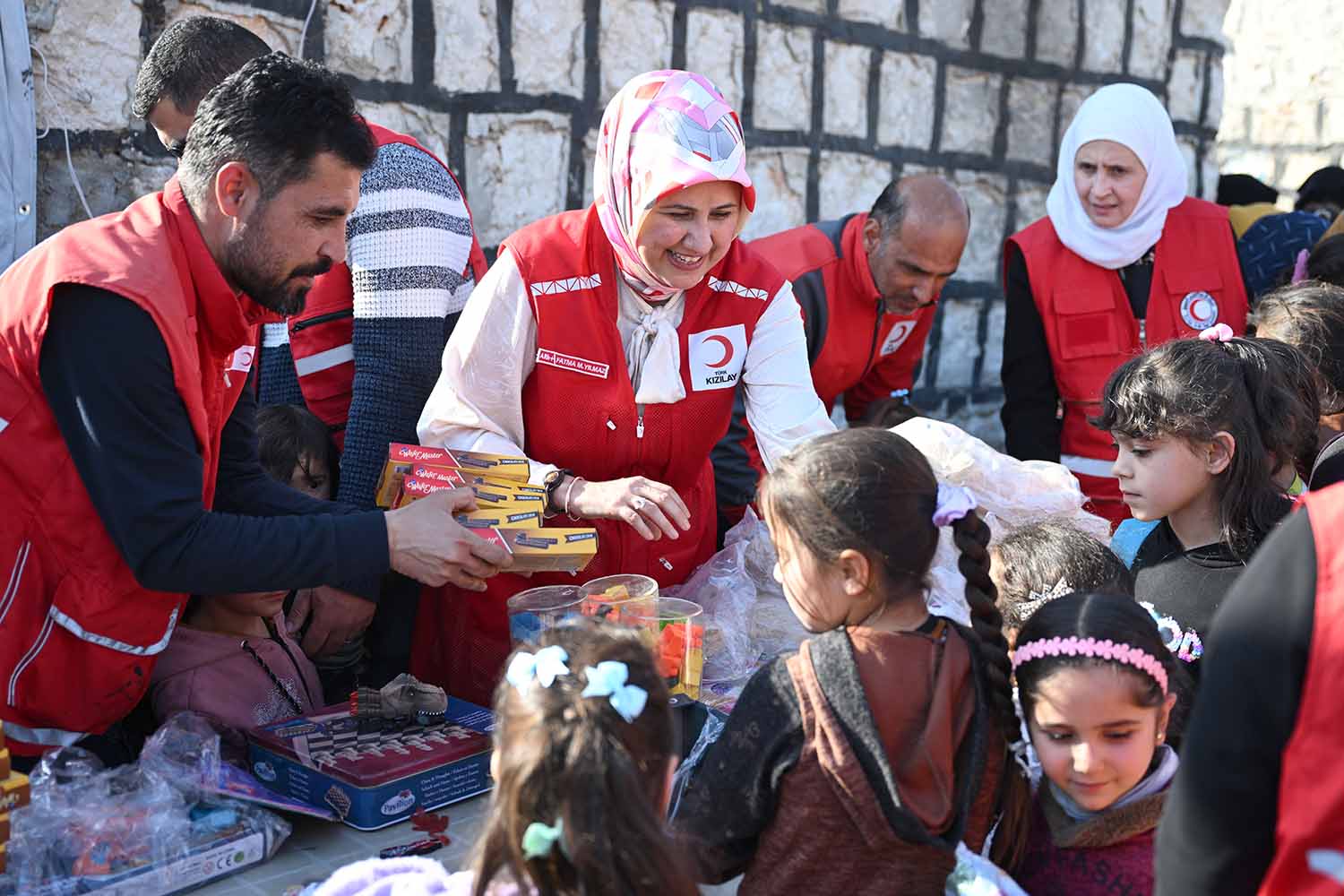 Men and women in Red Crescent uniforms give food items to a group of children.
