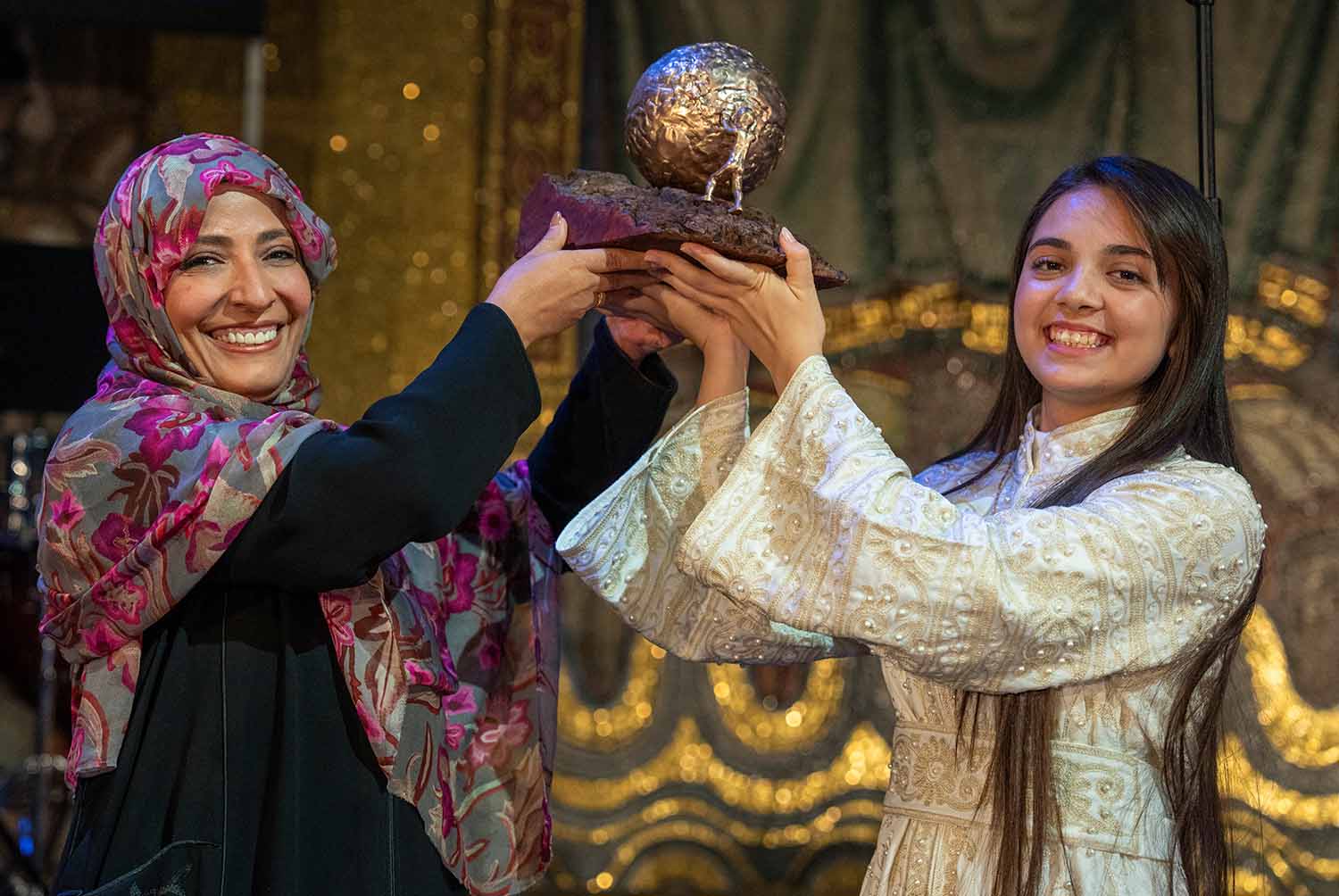 Tawakkol Karman and Bana Alabed smile as they lift Alabed’s peace award into the air together.