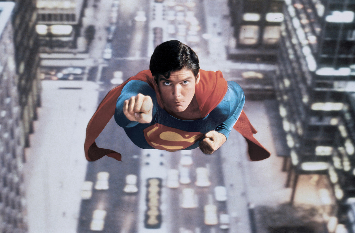 Christopher Reeve wears the Superman costume as he appears to fly over a city.
