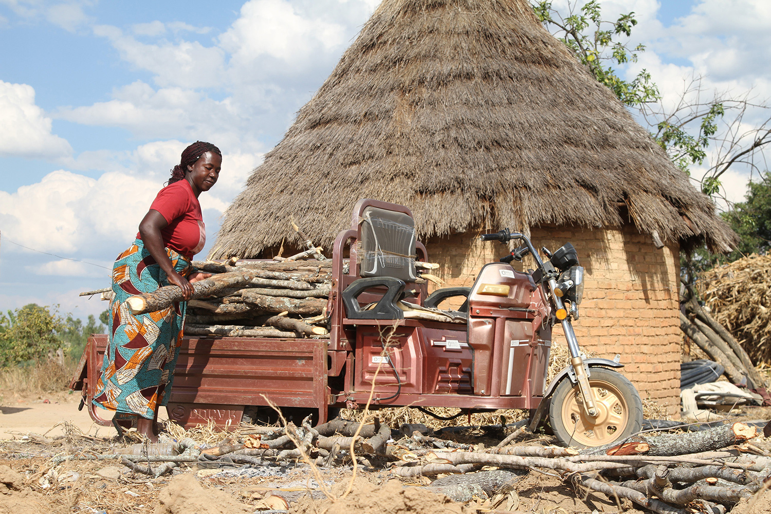 A woman unloads logs from the back of a three wheeled vehicle.