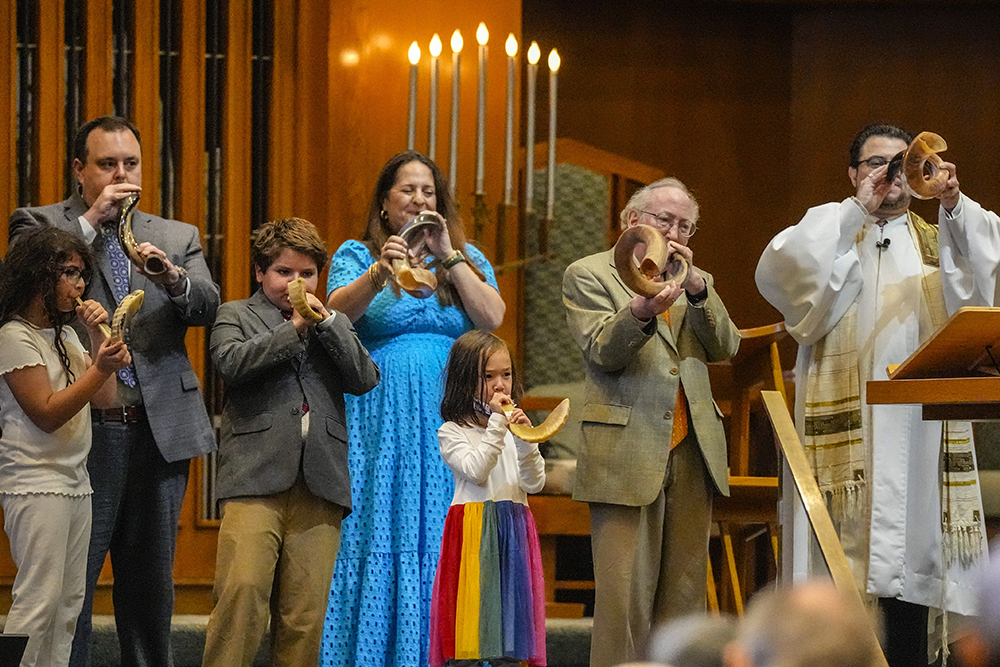 A family of six and a rabbi blow ram’s horns inside a synagogue.