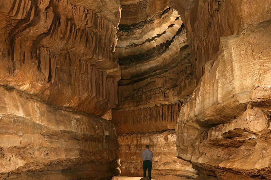 A man stands inside a large cave room.