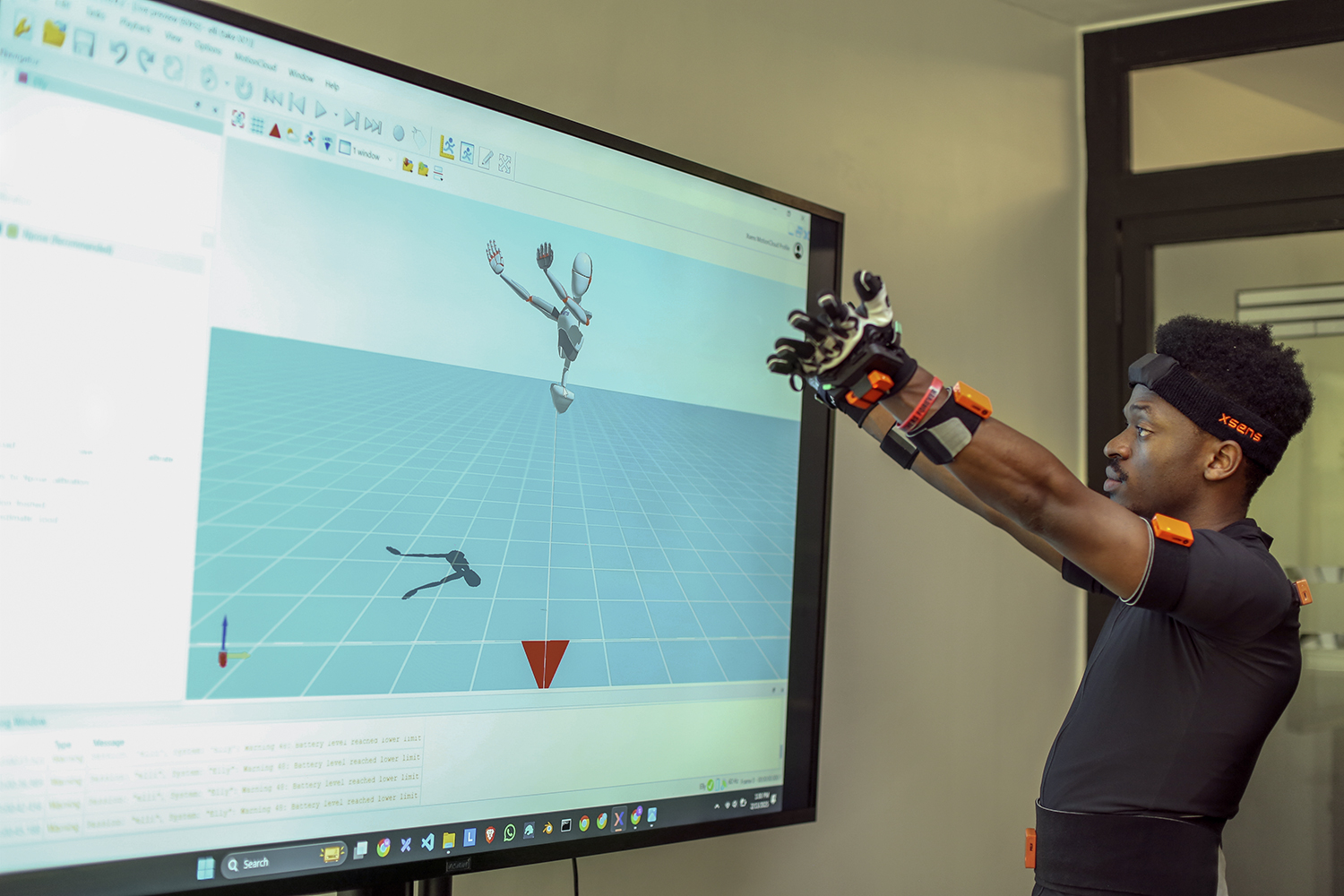 Elly Savatia stands in front of a screen and holds out his gloved hands while an avatar on the screen strikes the same pose.