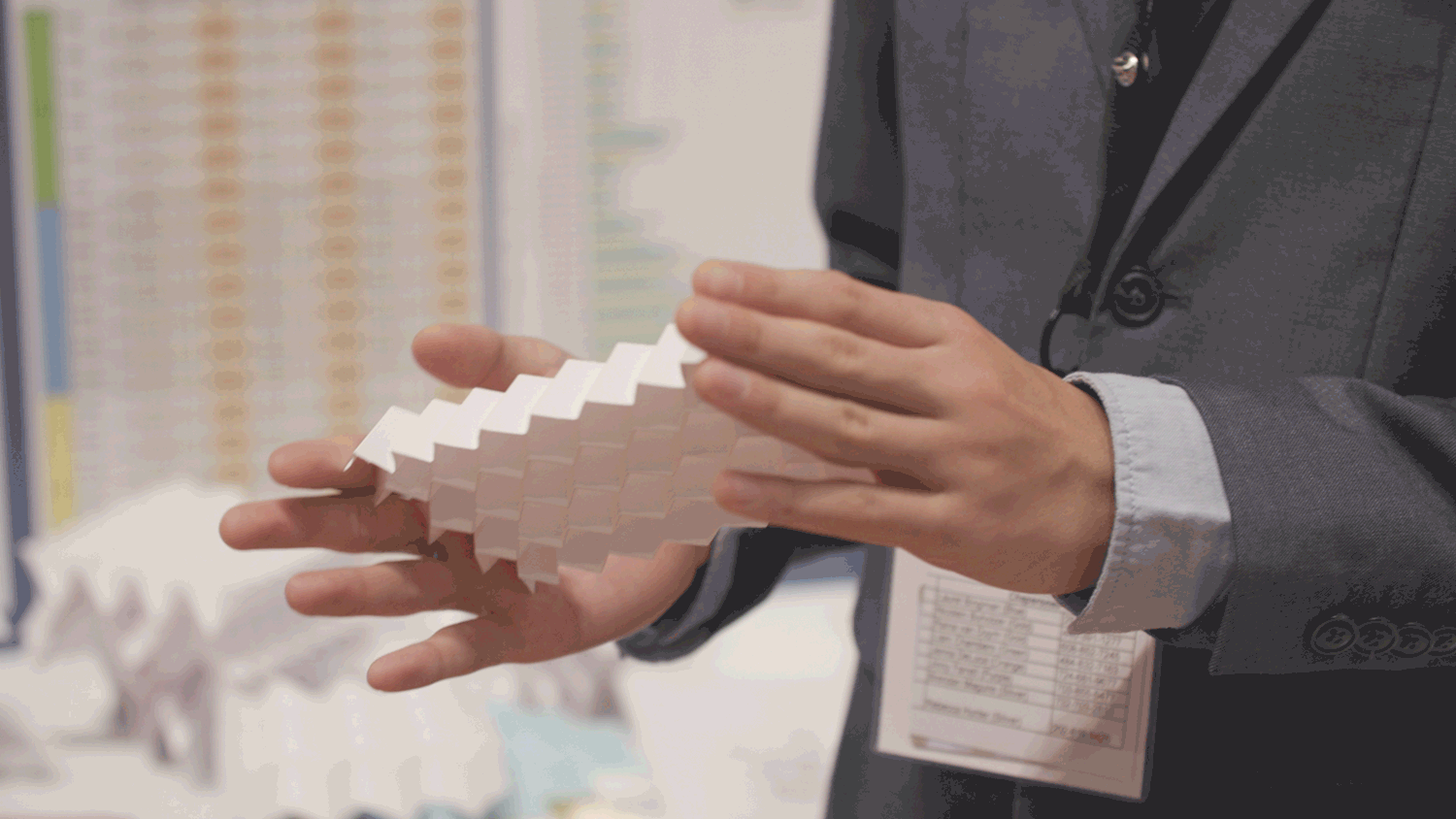 Two hands expand and contract a piece of paper that has been folded in the Miura-ori origami fold.