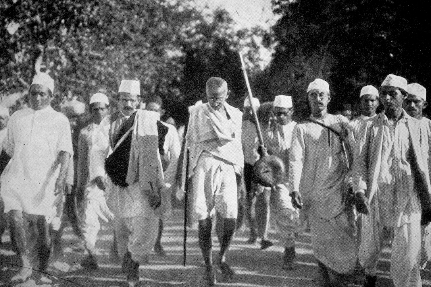 Mahatma Gandhi and several other men march down a street.