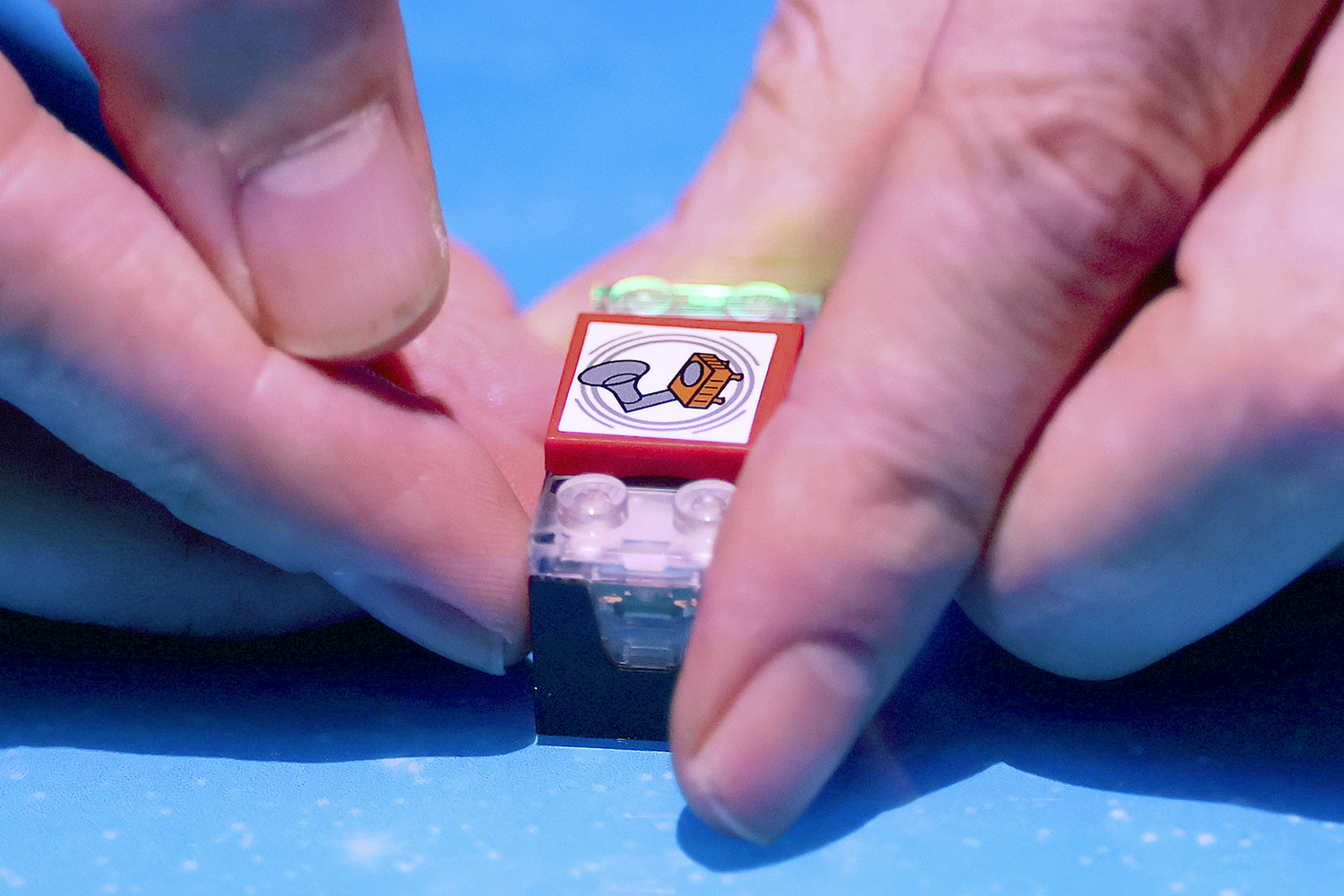 Two hands hold a lit up LEGO brick featuring an illustration of a speaker to indicate sound.