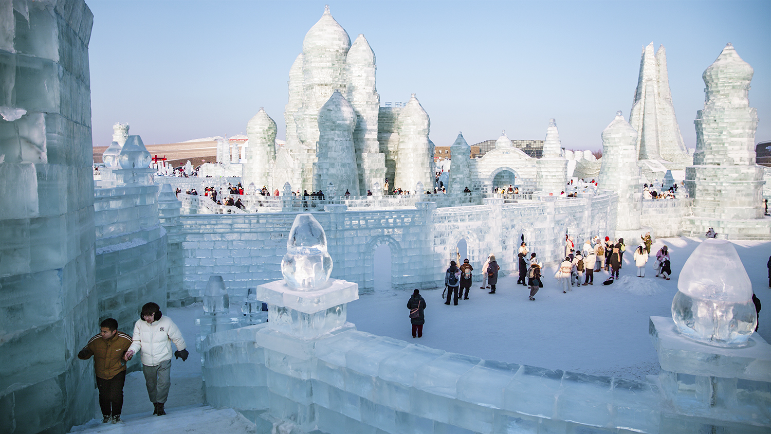 Several people stand and walk around an area where there are many walls and turrets constructed with bricks of ice.