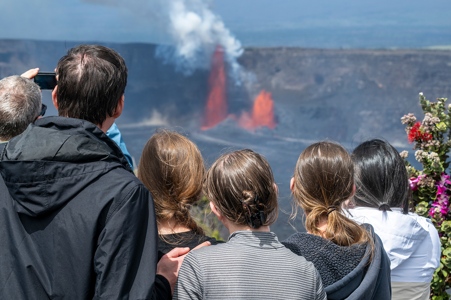 A view from behind of adults and children watching Kilauea during the day.