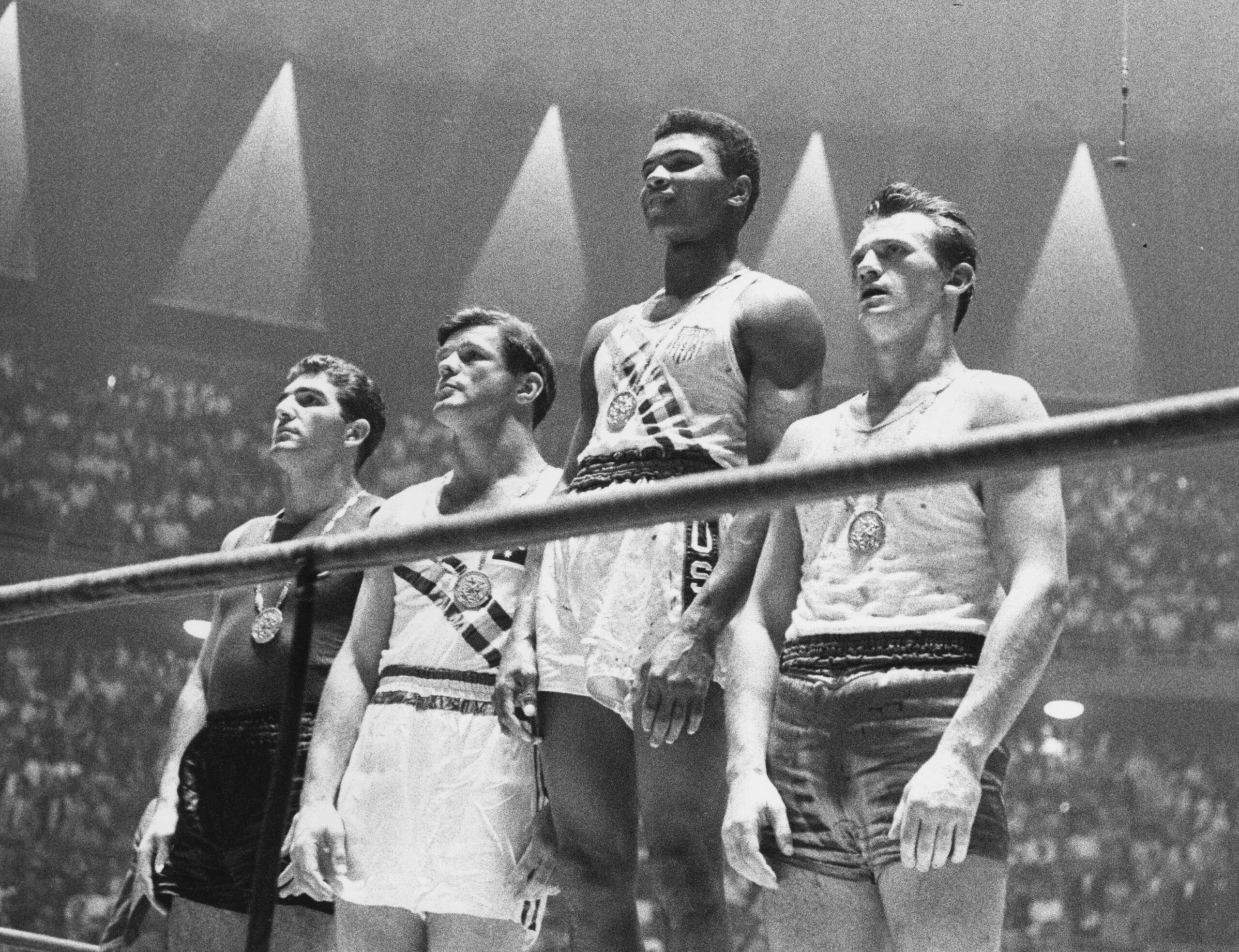 Muhammad Ali and the three other medal winning boxers stand on the Olympic podium while wearing their medals.