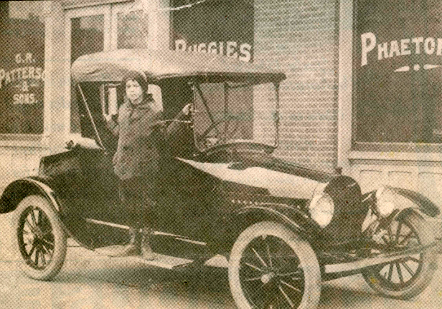 A young boy poses on the running board of a Patterson-Greenfield automobile in the early 20th century.