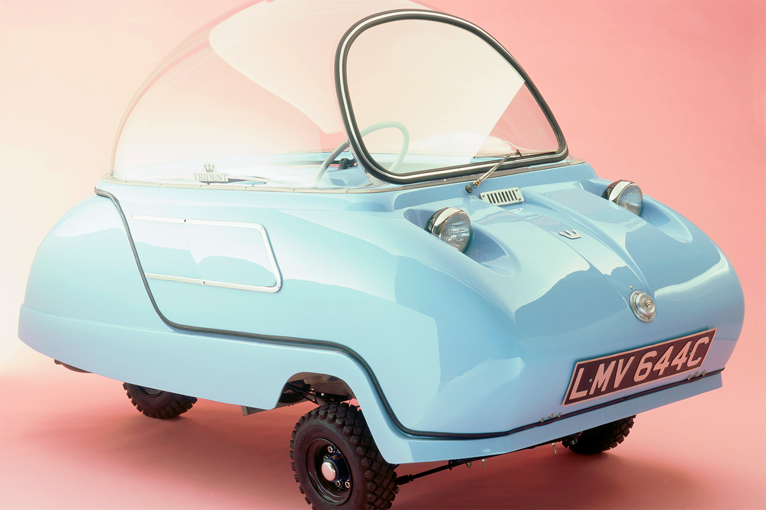 A blue car with a rounded glass top sits in a showroom.