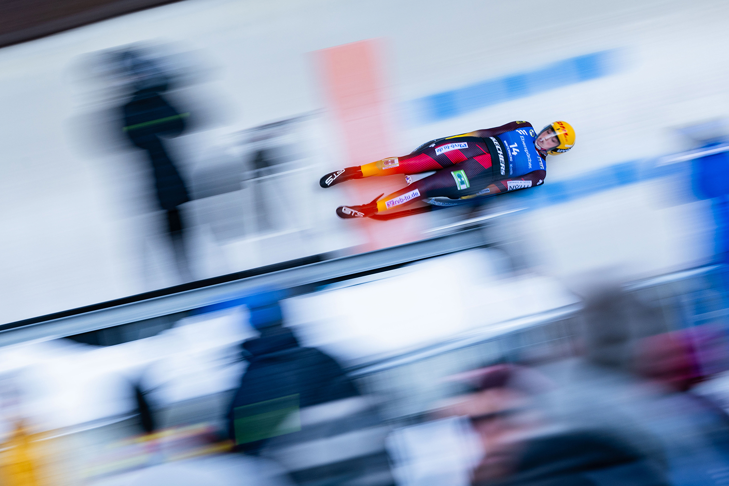 A luge competitor lies on her back on a luge sled and races down a track, making the background blurry.