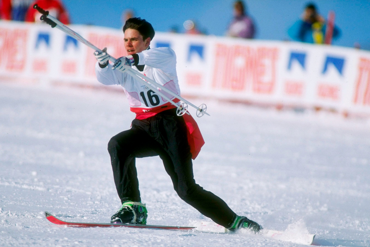 A man wearing skis holds out two poles while in a lunge position on a slope.
