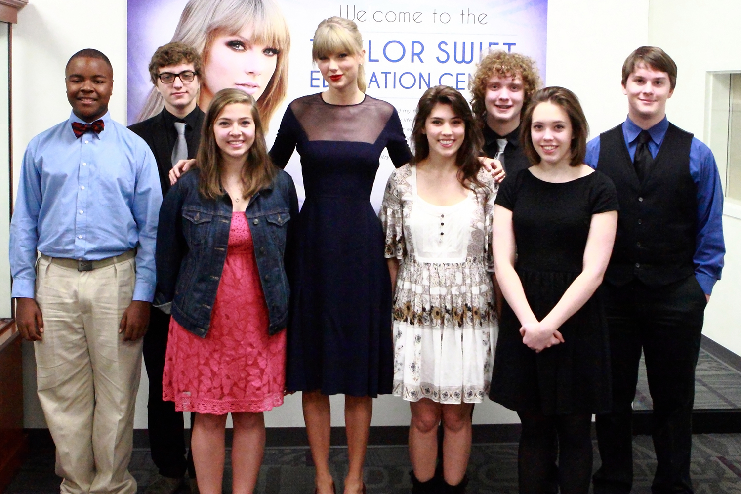 Taylor Swift poses for a photo with seven high school students in front of a sign reading Welcome to the Taylor Swift Education Center.