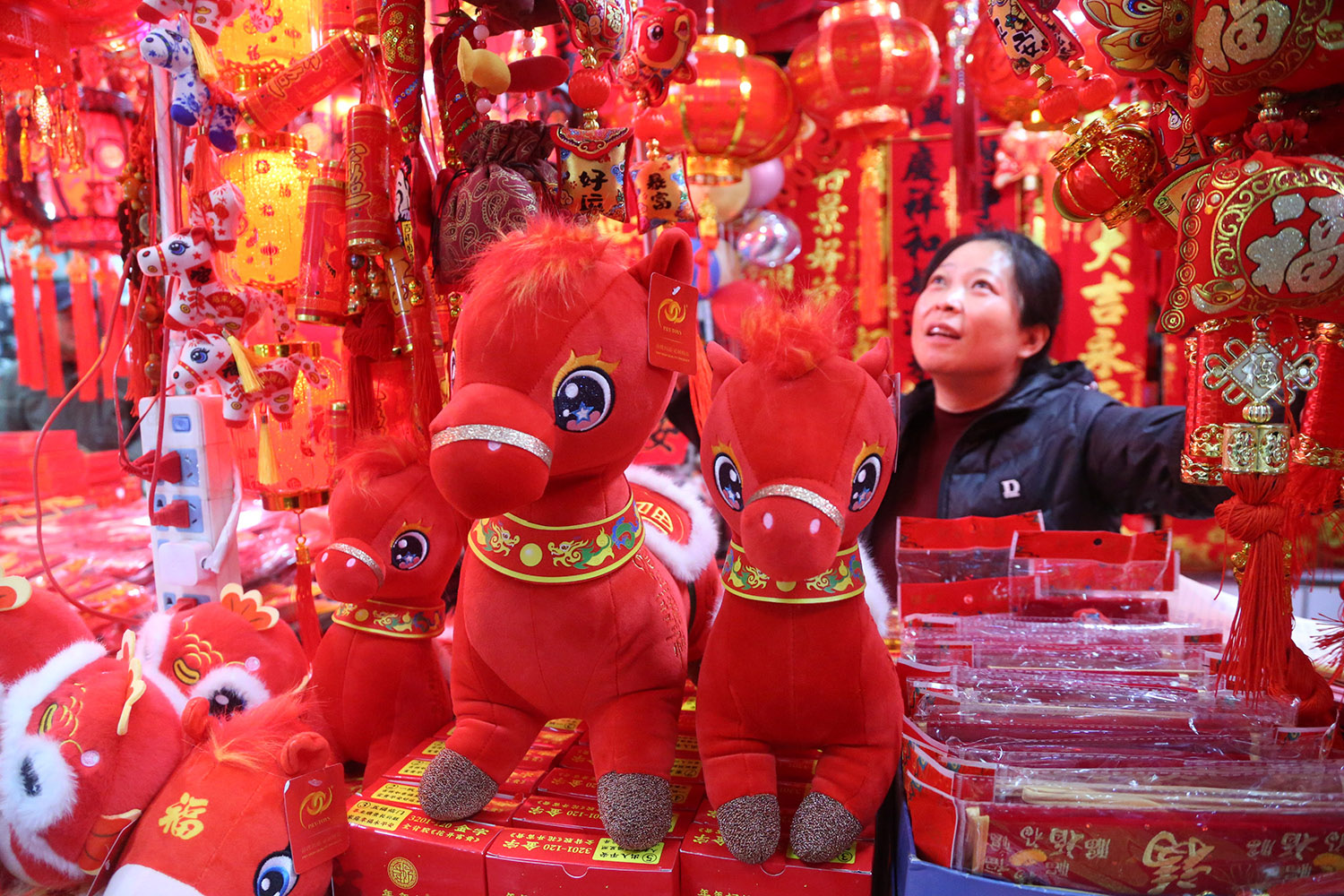 A woman stands in a store that is filled with red lanterns, red stuffed horses, and other red items.