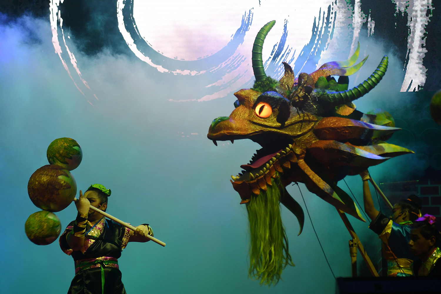 A performer manipulates the head of a monster resembling a dragon as another performer manipulates another object.