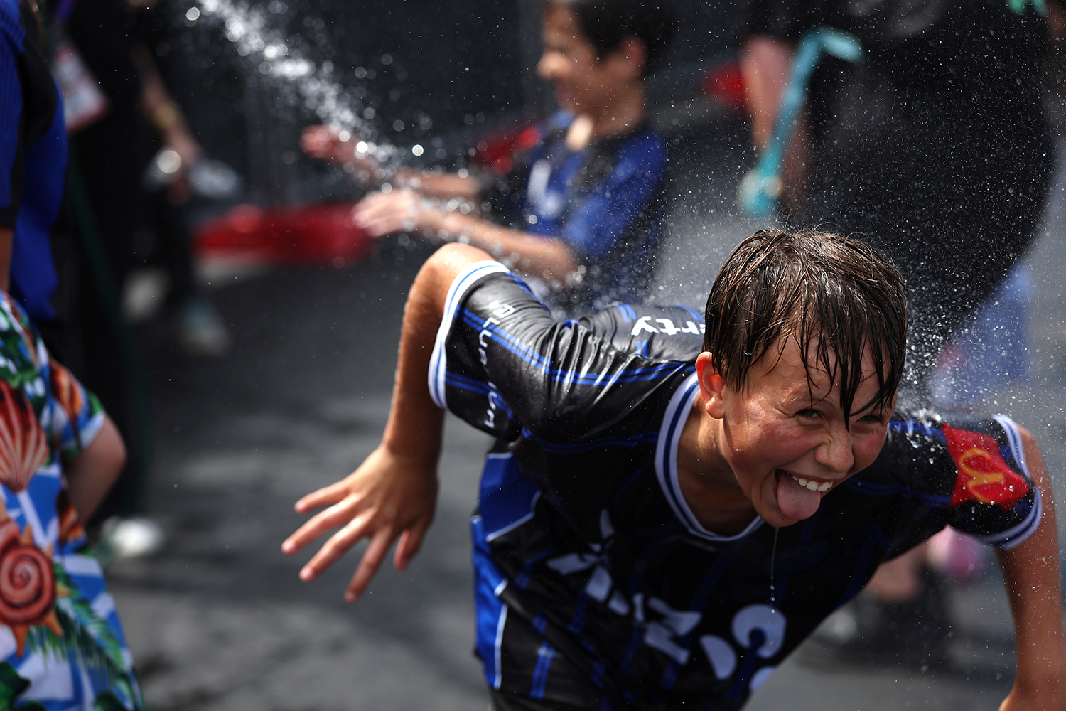 A child smiles during a water fight while running away from water that appears to be coming from a Super Soaker or similar toy.