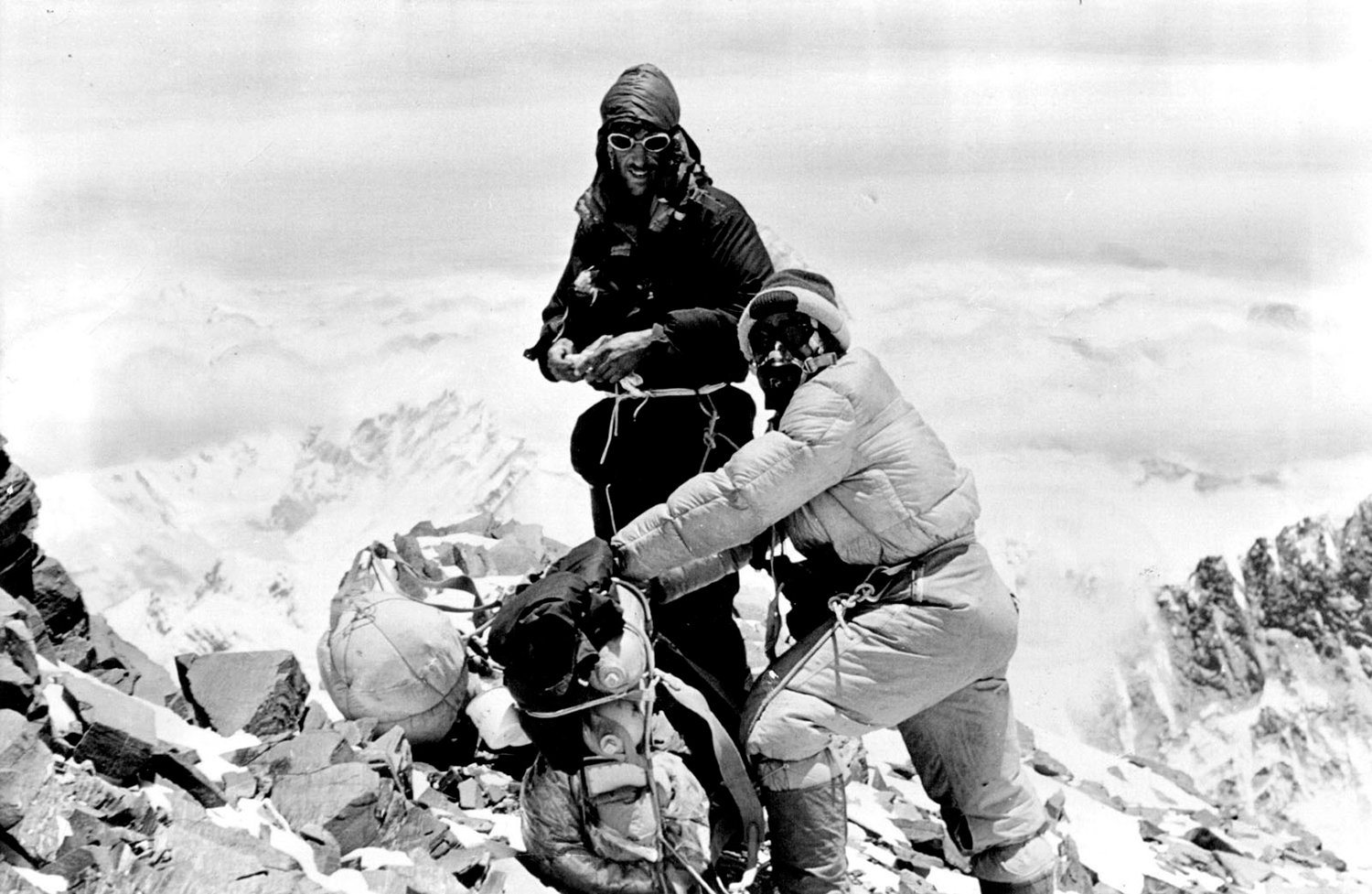 Edmund Hillary and Tenzing Norgay stand on the side of Mount Everest with their equipment.