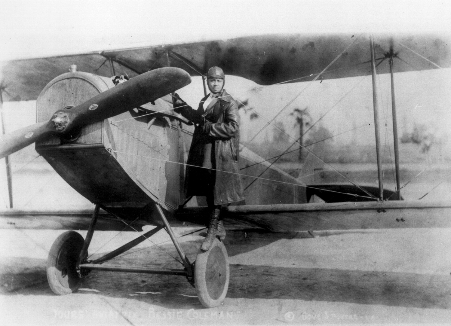 Bessie Coleman stands on the wheel of her biplane.