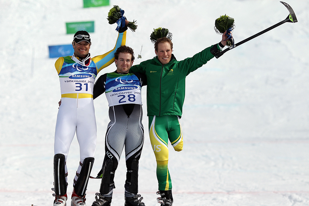 Three skiers pose on a snowy slope with two skiers holding their arms up.