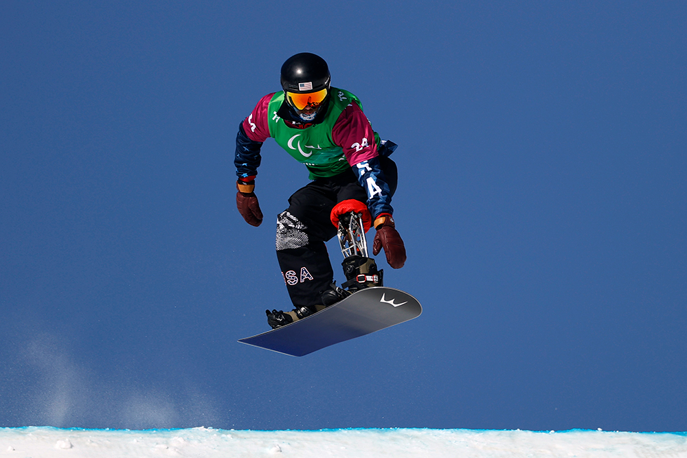 A snowboarder with a prosthetic leg is on a snowboard and in the air.