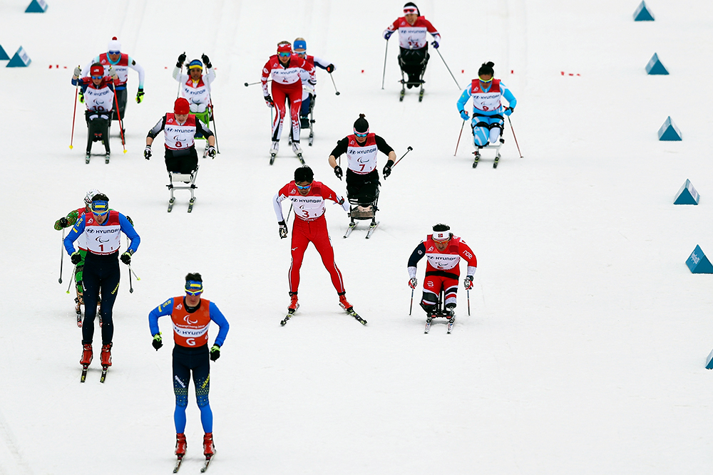 Several skiers, some sitting and others standing, ski down a hill.