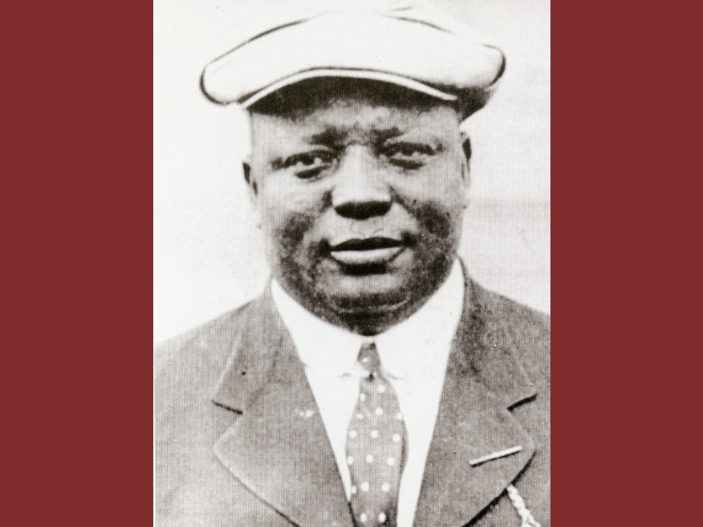 Rube Foster wears a suit and cap in a portrait.