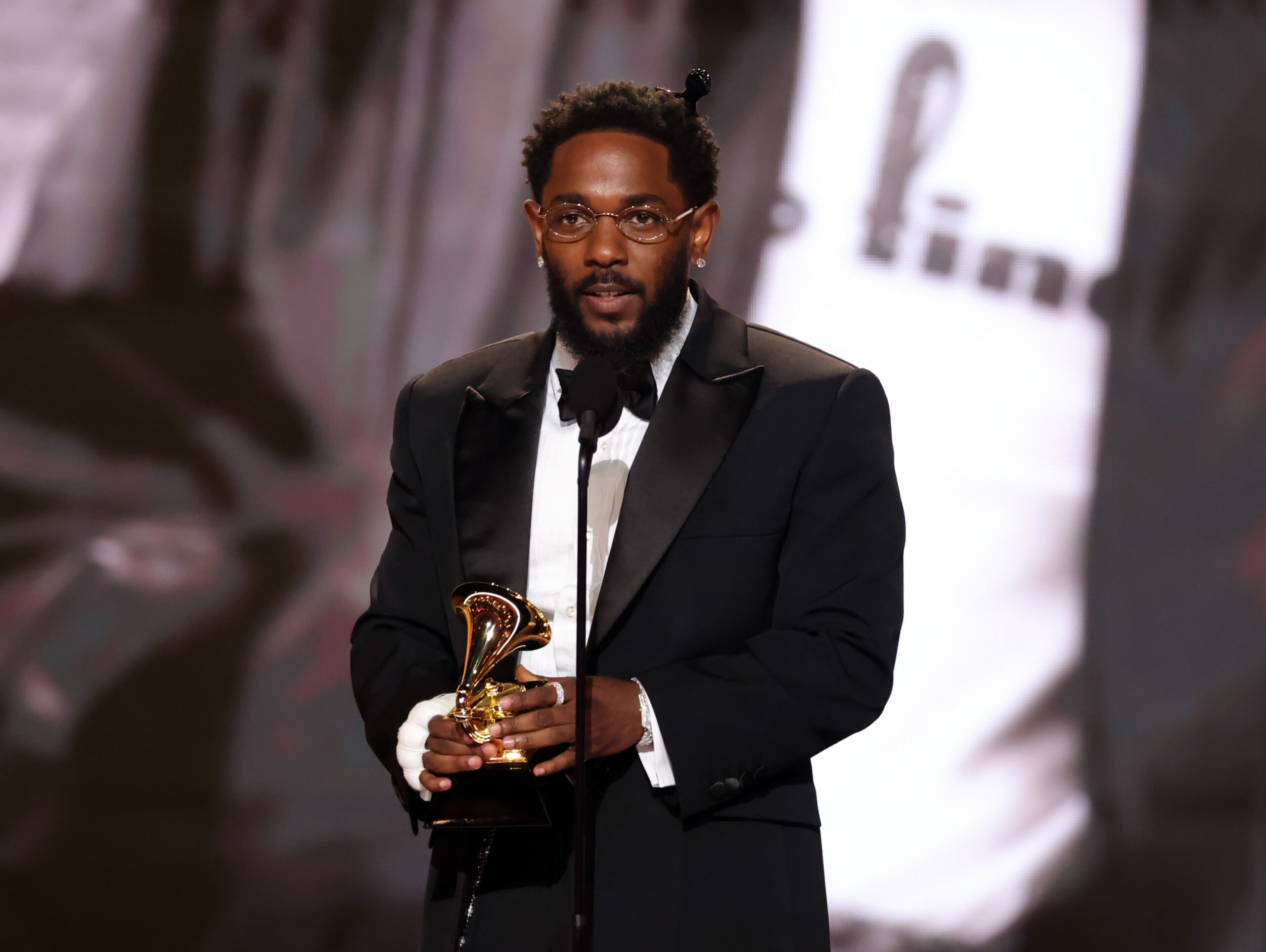 Kendrick Lamar stands at a microphone while holding a Grammy Award.