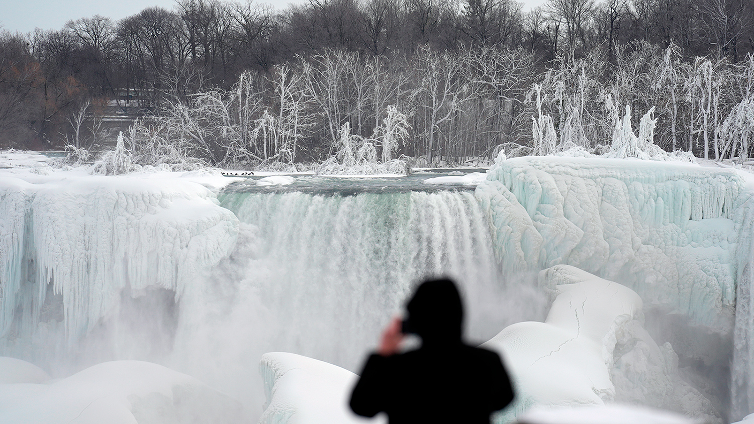 A person takes a photo of the partially frozen Niagara Falls.
